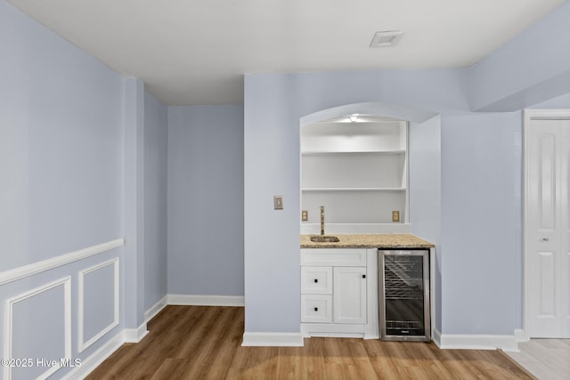 bar featuring white cabinetry, sink, light stone counters, hardwood / wood-style floors, and beverage cooler