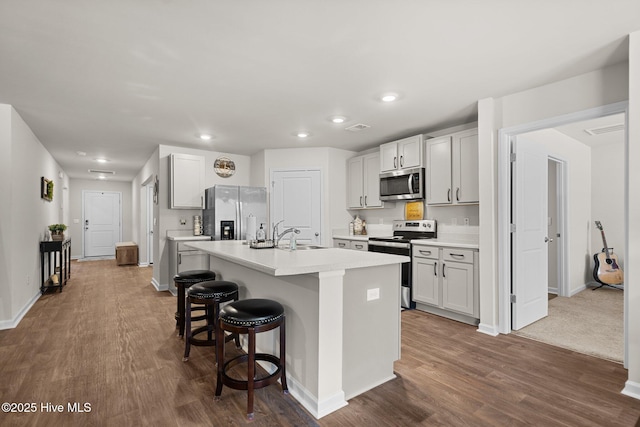 kitchen with a kitchen island with sink, dark wood-type flooring, stainless steel appliances, and a kitchen breakfast bar