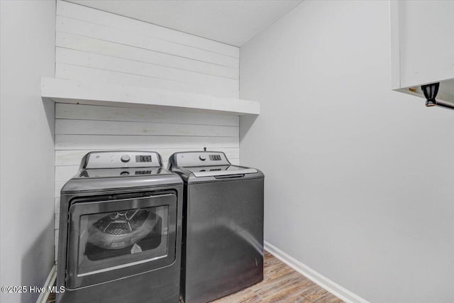 laundry room with hardwood / wood-style floors, wooden walls, and washing machine and dryer