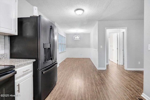 kitchen featuring white cabinets, hanging light fixtures, black appliances, a textured ceiling, and light hardwood / wood-style flooring