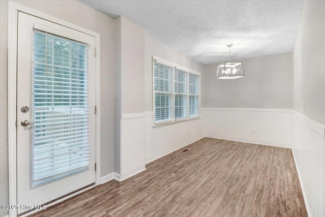 empty room featuring wood-type flooring, a chandelier, and a textured ceiling