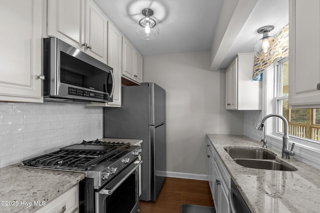 kitchen with baseboards, light stone counters, a sink, appliances with stainless steel finishes, and white cabinets