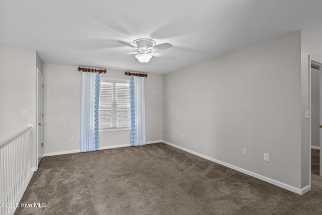 empty room with a ceiling fan, dark colored carpet, and baseboards