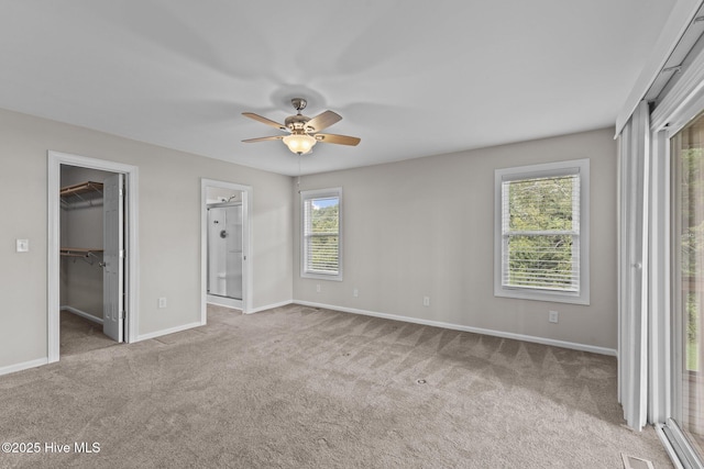 unfurnished bedroom with visible vents, a walk in closet, baseboards, light carpet, and ceiling fan