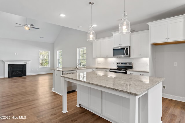 kitchen with stainless steel appliances, a peninsula, white cabinets, open floor plan, and a center island