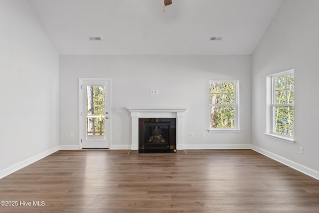 unfurnished living room with a fireplace with flush hearth, visible vents, vaulted ceiling, and wood finished floors