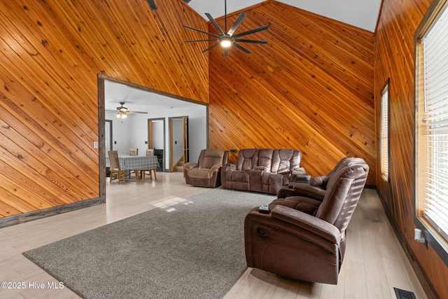 living area featuring visible vents, a ceiling fan, wood finished floors, wooden walls, and a high ceiling