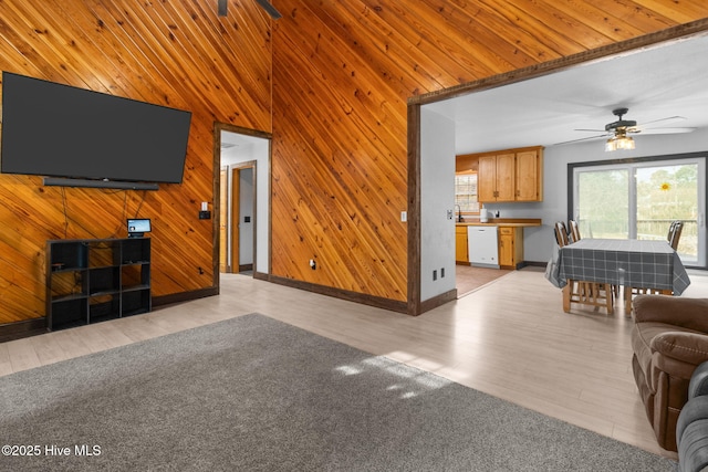 unfurnished living room with plenty of natural light, wood walls, a ceiling fan, and light wood finished floors