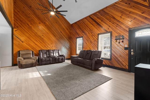 living room with light wood-style floors, high vaulted ceiling, ceiling fan, and wood walls