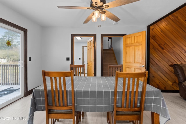 dining area with stairway, a ceiling fan, baseboards, light wood-style flooring, and wood walls