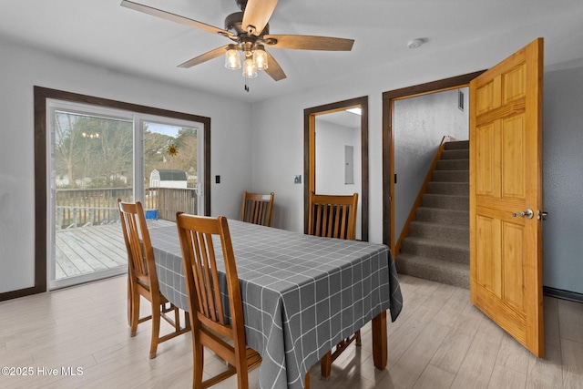 dining area featuring electric panel, stairway, light wood-style flooring, and a ceiling fan