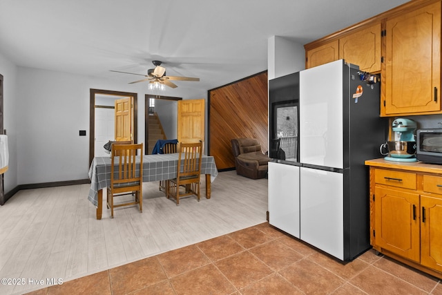 kitchen with freestanding refrigerator, ceiling fan, light countertops, wood walls, and brown cabinets