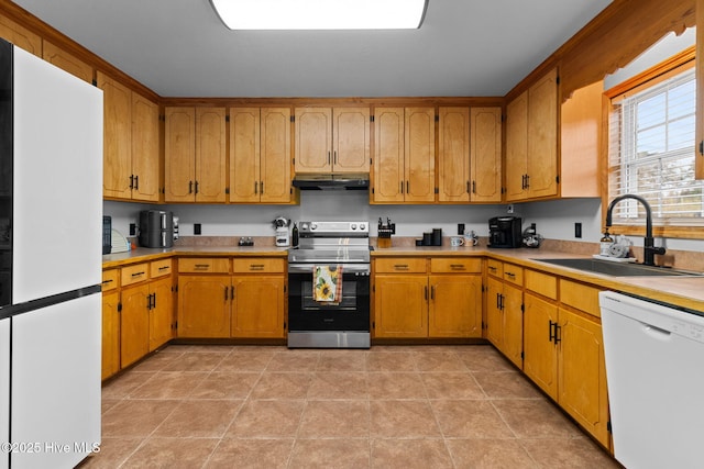 kitchen with brown cabinets, a sink, under cabinet range hood, white appliances, and light countertops