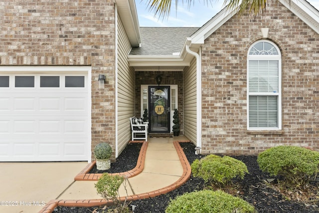 entrance to property featuring brick siding, an attached garage, and roof with shingles