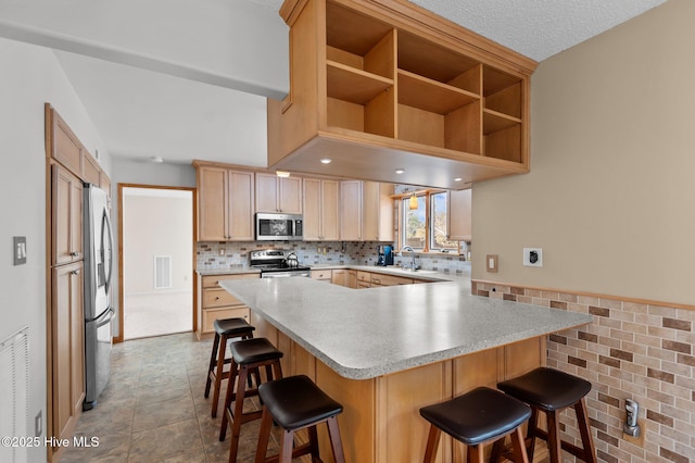 kitchen featuring visible vents, a kitchen breakfast bar, stainless steel appliances, a peninsula, and light countertops