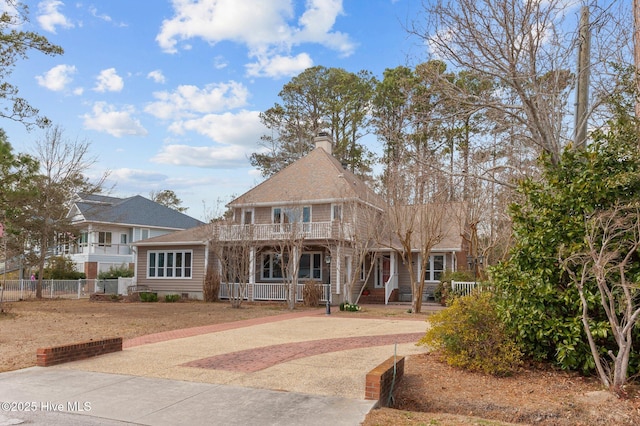 view of front facade with covered porch, driveway, fence, and a balcony