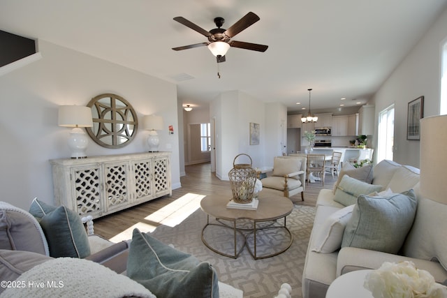 living room featuring ceiling fan with notable chandelier and light hardwood / wood-style flooring