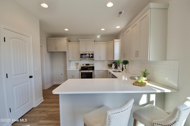 kitchen with appliances with stainless steel finishes, wood-type flooring, sink, a breakfast bar area, and kitchen peninsula