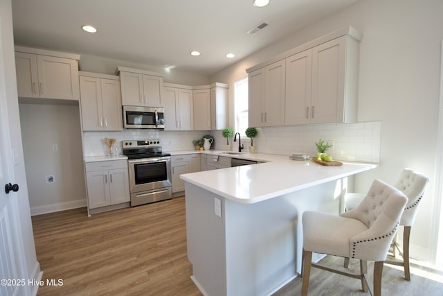 kitchen with stainless steel appliances, light hardwood / wood-style flooring, a kitchen breakfast bar, and kitchen peninsula