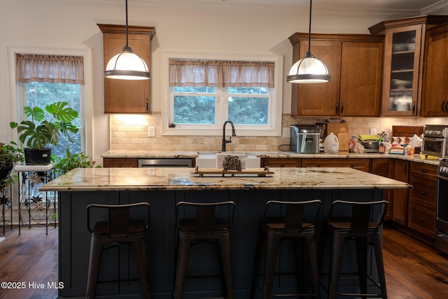 kitchen with brown cabinetry, a kitchen island, glass insert cabinets, a breakfast bar area, and pendant lighting