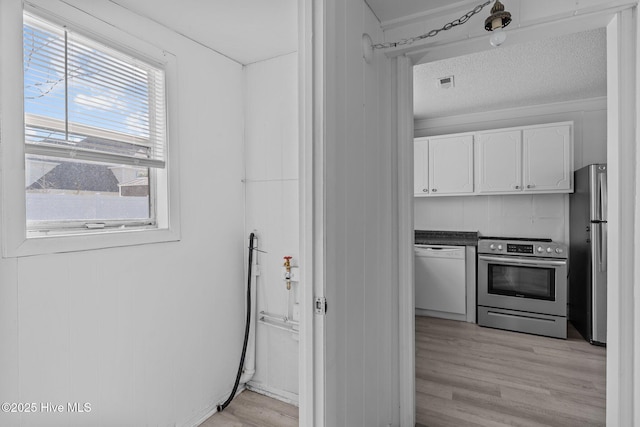 kitchen featuring appliances with stainless steel finishes, a textured ceiling, decorative backsplash, light wood-type flooring, and white cabinetry