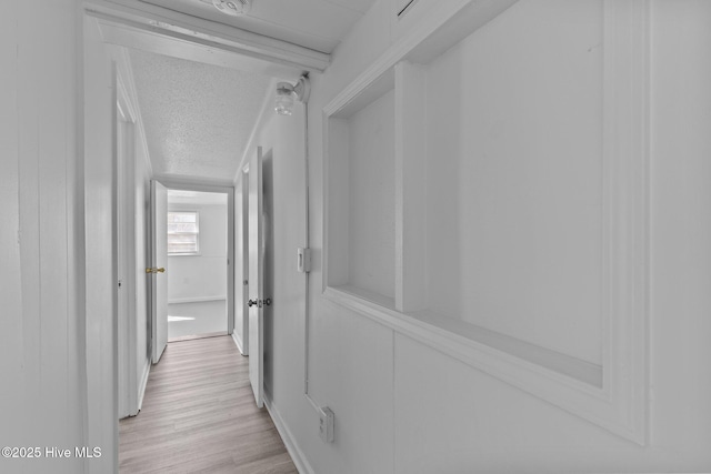 hall with light wood-type flooring and a textured ceiling