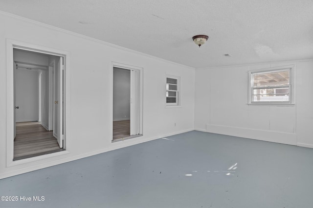 empty room with a textured ceiling, ornamental molding, and concrete flooring