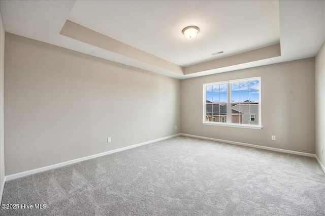 empty room featuring carpet flooring, visible vents, a tray ceiling, and baseboards