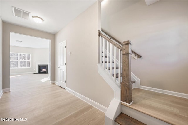 staircase featuring a fireplace with flush hearth, wood finished floors, baseboards, and visible vents