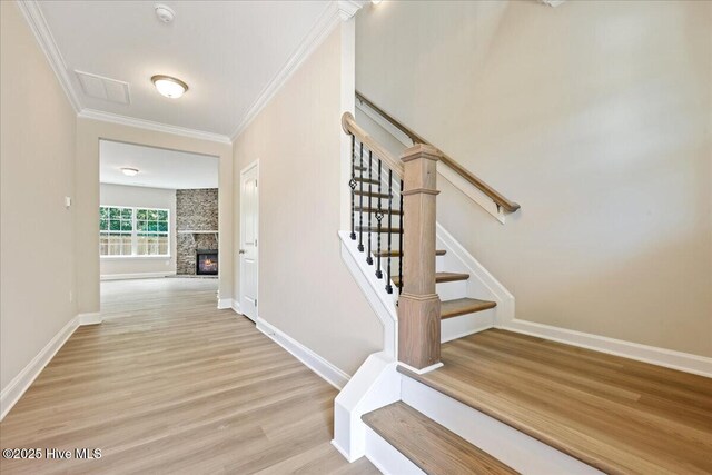 stairway with crown molding, baseboards, a stone fireplace, and wood finished floors