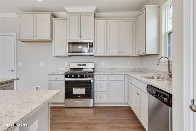 kitchen with a sink, light wood-style flooring, appliances with stainless steel finishes, and light stone counters