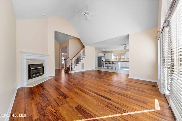 unfurnished living room featuring ceiling fan, high vaulted ceiling, wood-type flooring, and a fireplace