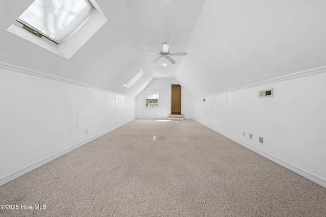 additional living space featuring light carpet, vaulted ceiling with skylight, and ceiling fan