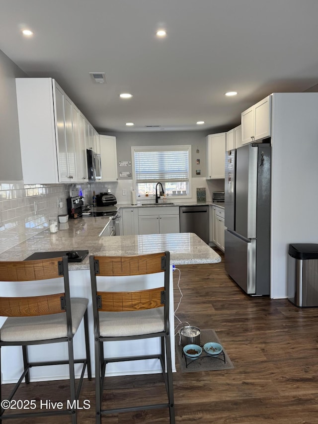 kitchen with decorative backsplash, dark wood-style floors, a peninsula, stainless steel appliances, and a sink