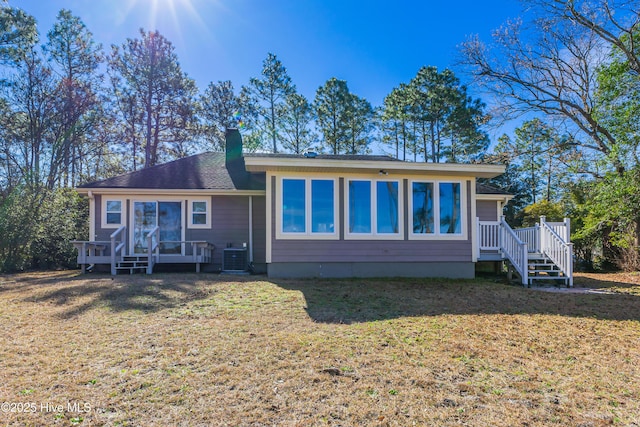 rear view of house with a deck, a chimney, a yard, and cooling unit