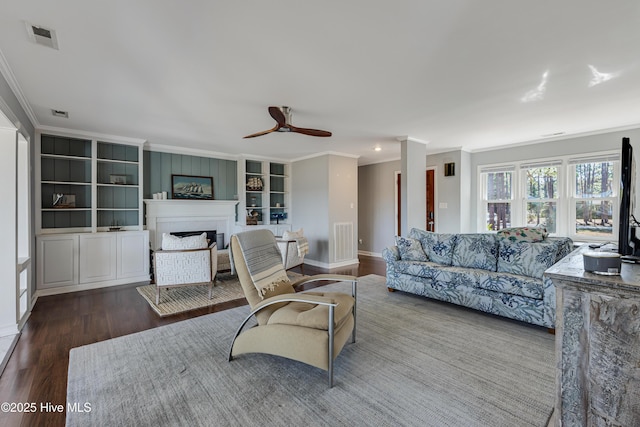 living area with a fireplace, wood finished floors, ornamental molding, and visible vents