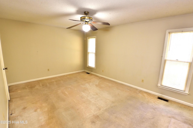 empty room featuring ceiling fan, visible vents, and a wealth of natural light