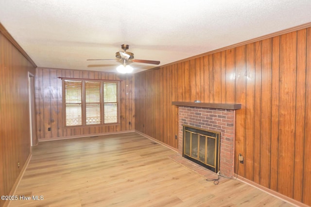 unfurnished living room featuring light wood-style flooring, wooden walls, a fireplace, and a ceiling fan