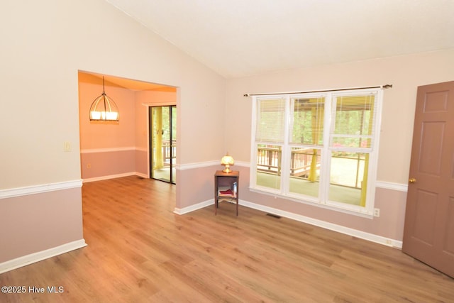 spare room with a chandelier, light wood-style floors, baseboards, and lofted ceiling