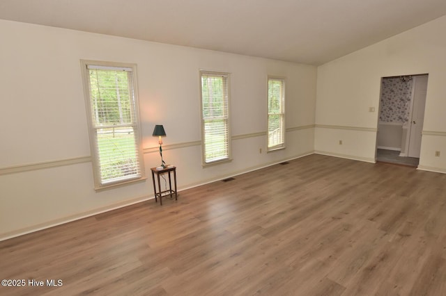 unfurnished room featuring a wealth of natural light, wood finished floors, and vaulted ceiling