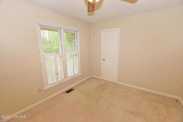 empty room with visible vents, light colored carpet, baseboards, and ceiling fan