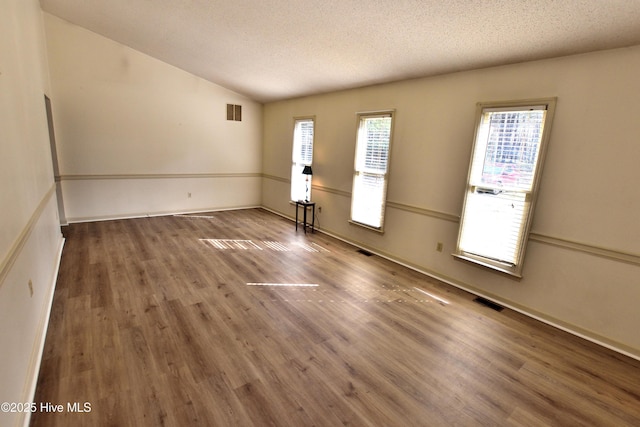 spare room with visible vents, baseboards, a textured ceiling, wood finished floors, and lofted ceiling