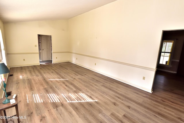spare room featuring wood finished floors, baseboards, and lofted ceiling