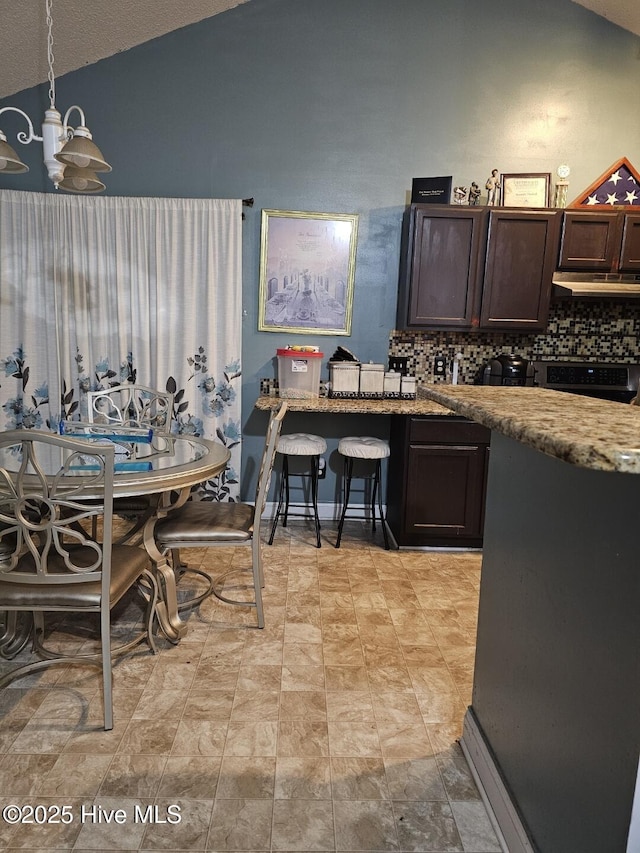 kitchen featuring vaulted ceiling, light stone countertops, pendant lighting, and dark brown cabinetry