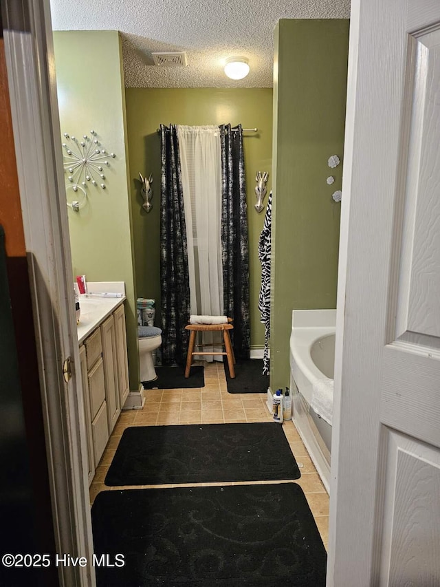 bathroom featuring toilet, a textured ceiling, vanity, a bathing tub, and tile patterned flooring