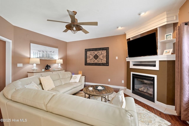 living area with a fireplace, wood finished floors, a ceiling fan, and baseboards