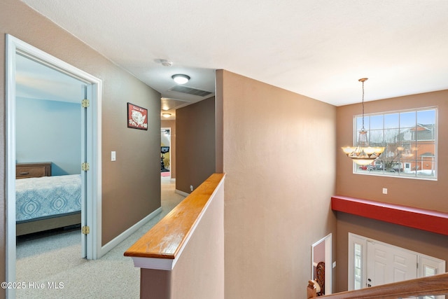 hallway featuring baseboards, visible vents, a notable chandelier, and an upstairs landing