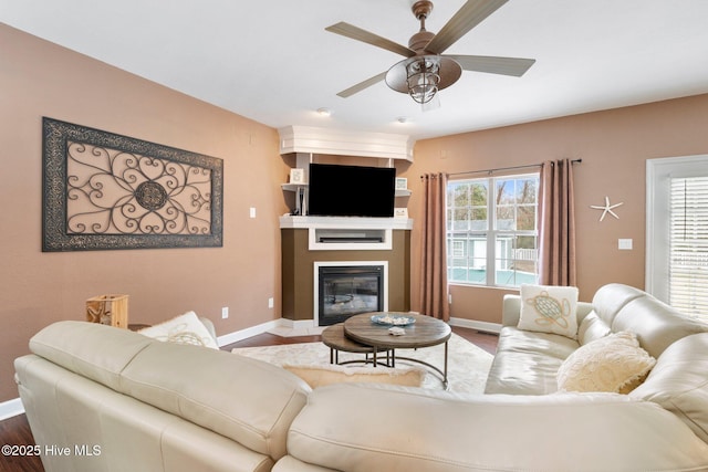 living room featuring a large fireplace, ceiling fan, wood finished floors, and baseboards