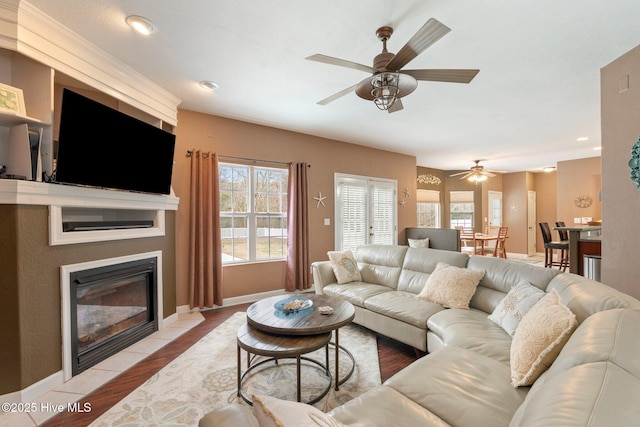 living room featuring a ceiling fan, baseboards, light wood-style flooring, and a tiled fireplace