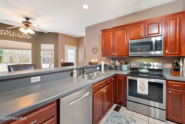 kitchen with light tile patterned floors, stainless steel appliances, dark countertops, and a sink